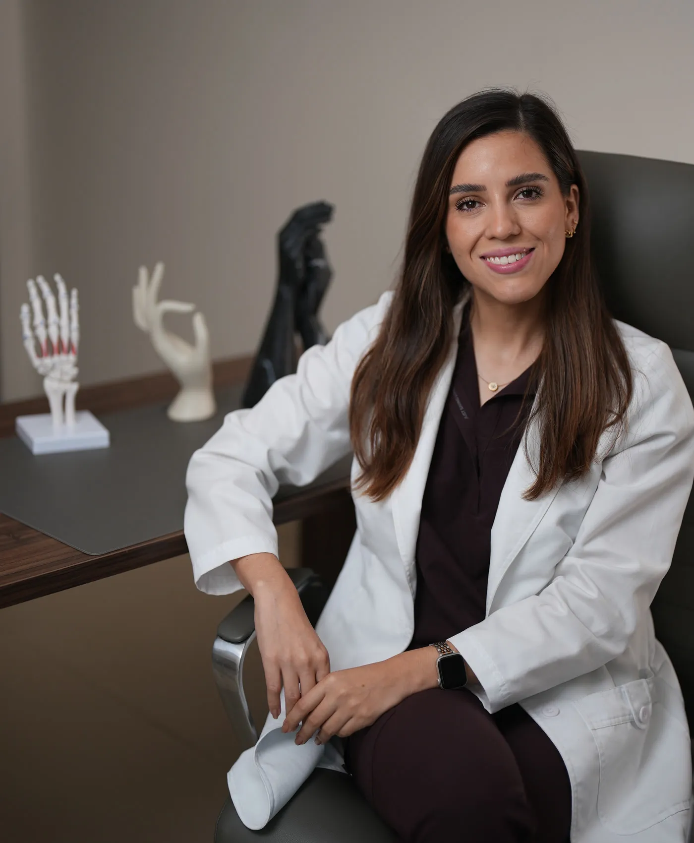 Dra. Catalina Larrazolo Ochoa, con bata blanca, sentada en su consultorio junto a modelos anatómicos de la mano